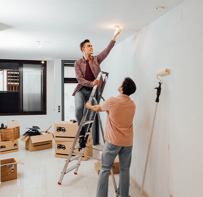 photo of a man up a ladder painting a celling whilst another man supports the ladder